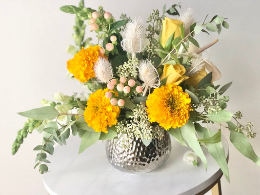 Bohemian style floral arrangement with Soft Orange, yellow, cream flowers with loose sage foliage in a luxury vase