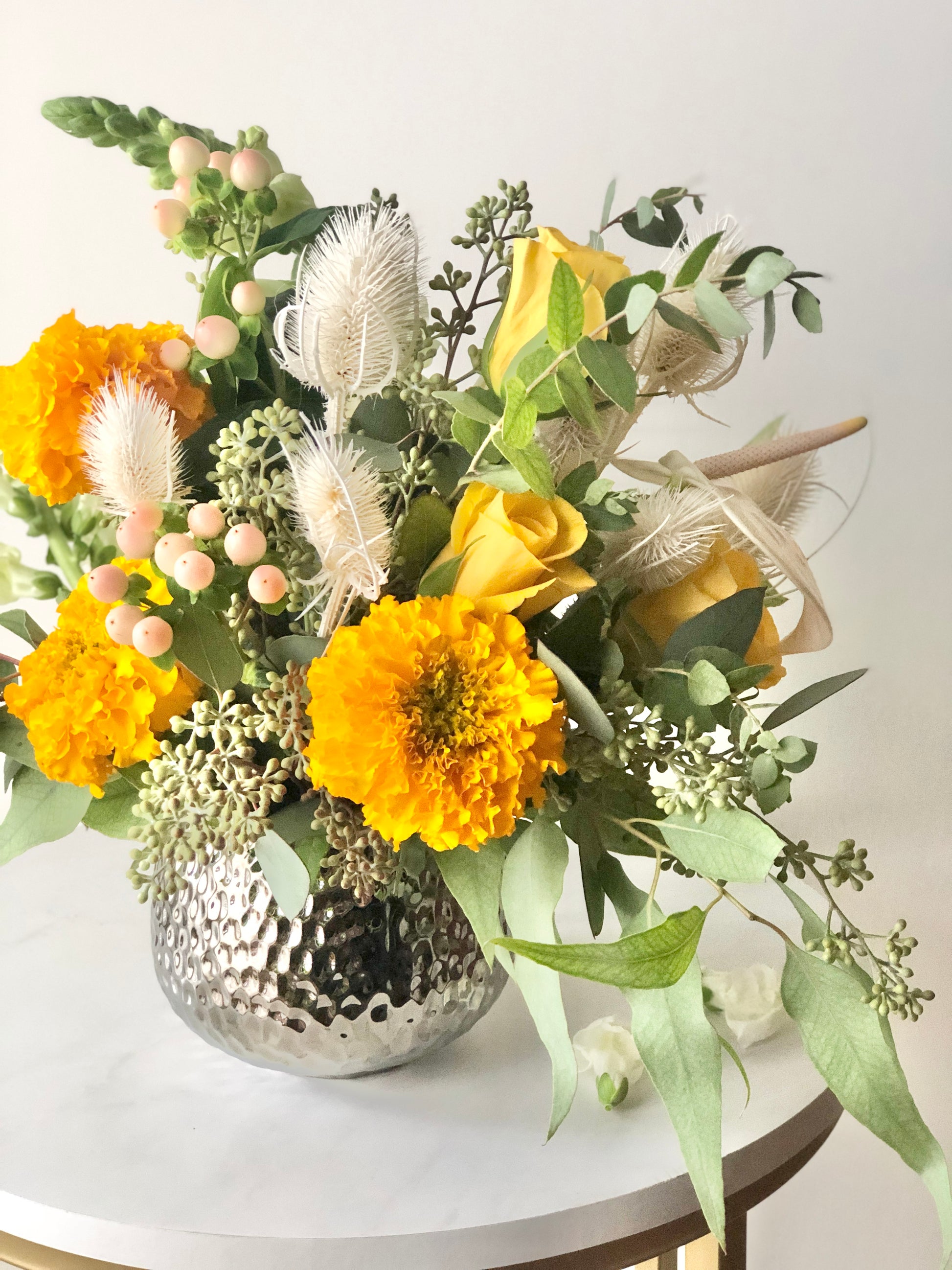 Side view of textured dried flowers in Bohemian style floral arrangement with Soft Orange, yellow, cream flowers with loose sage foliage in a luxury vase