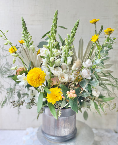 Large version of The Rambler, a Bohemian style floral arrangement with Soft Orange, yellow, cream flowers with loose sage foliage and dried palm fronds and orchids, in a luxury vase
