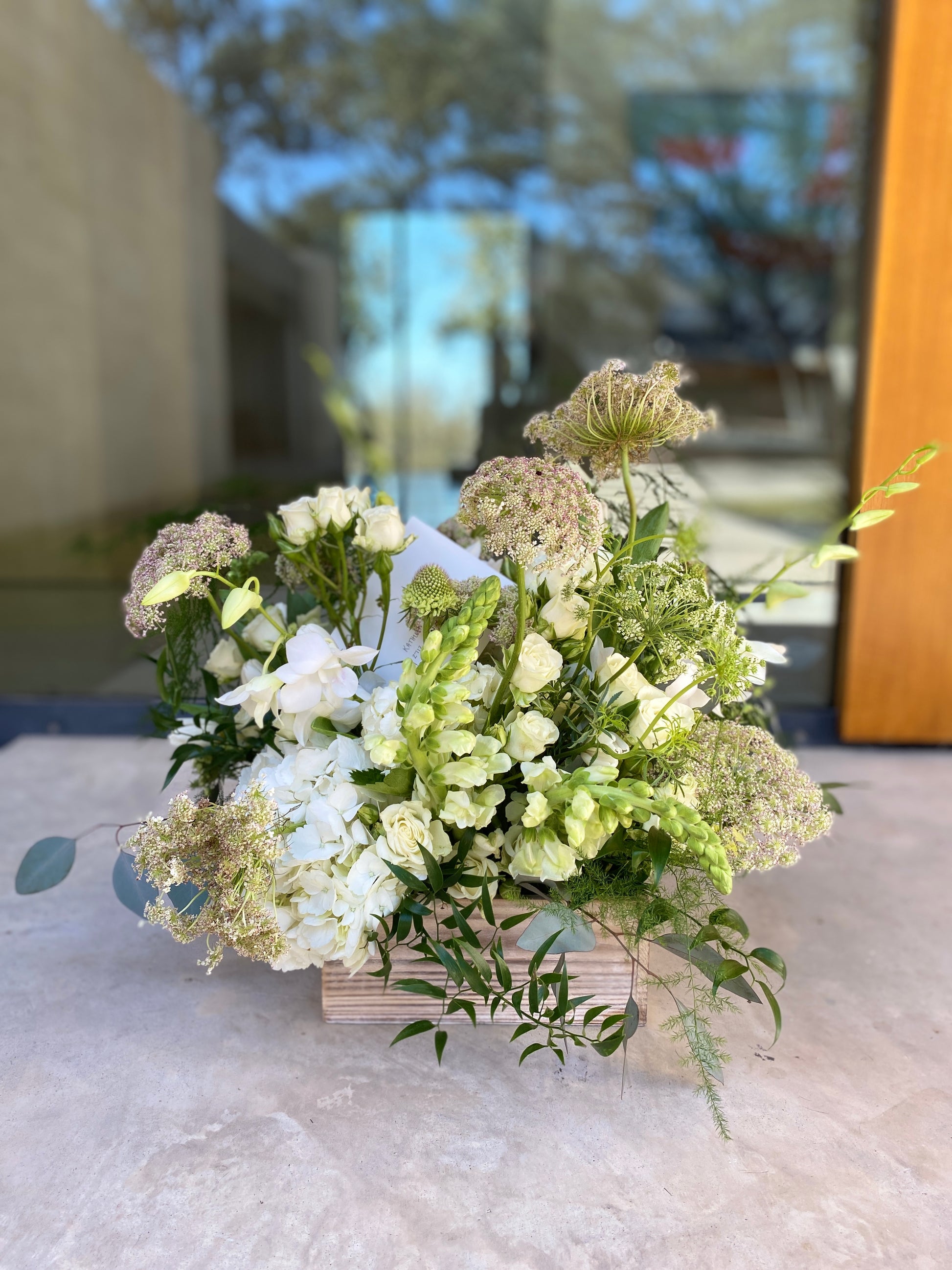 Real life image of Delivery of Barton Creek Gardens box garden of white and green flowers in front of modern glass door